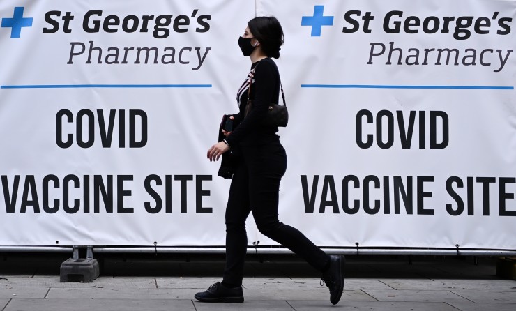 Una mujer pasea frente a un cartel de vacunación contra la COVID-19 en Londres (Reino Unido).